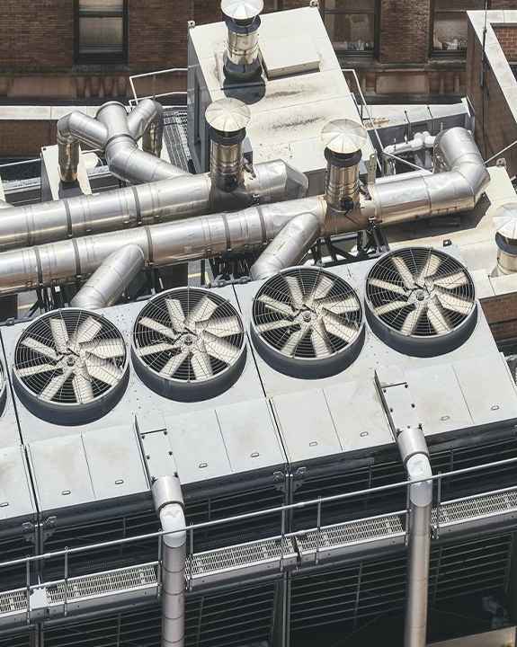A rooftop industrial HVAC system with four large fans and interconnected metal ducts sits atop a building, highlighting the importance of regular maintenance and timely AC repair.
