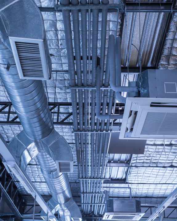 Exposed HVAC ducts, vents, and pipes on an industrial ceiling with metallic insulation panels highlight the need for regular ac repair and maintenance.