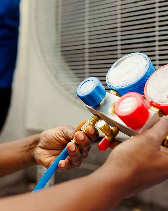 Person adjusting pressure gauges on HVAC equipment near an air conditioning unit during an ac repair.