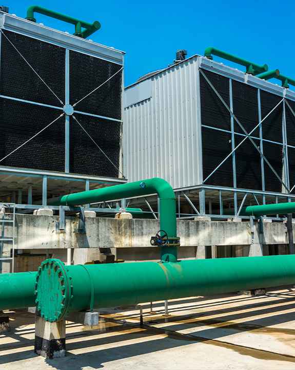 Two large industrial cooling towers with green pipes installed in front of them, set outdoors under a clear blue sky, highlight the scale of commercial ac repair and maintenance needs.